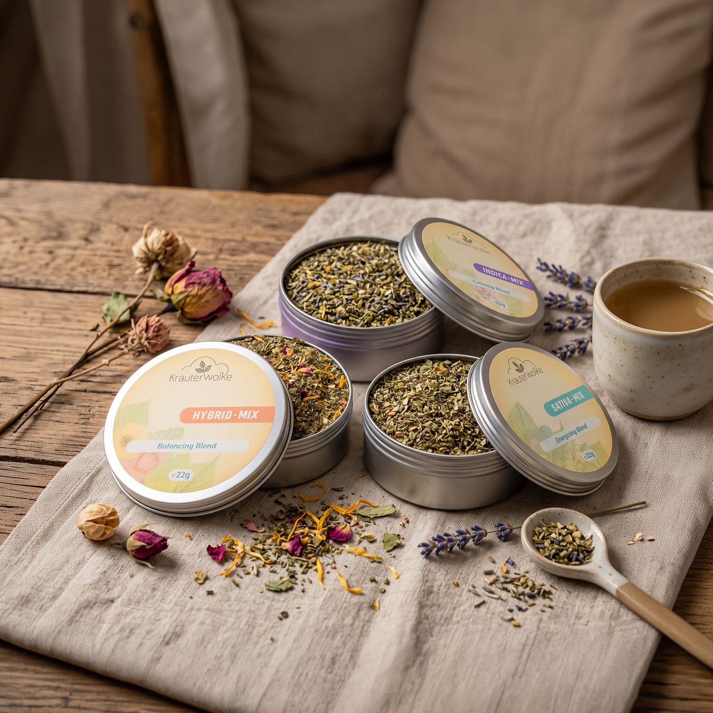 Drei geöffnete Kräuterwolke-Dosen – Hybrid, Indica und Sativa Mix – auf einem Leinentuch, daneben Rosenknospen, Lavendel und eine Tasse Tee